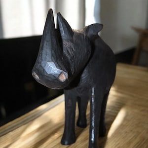 以下が含まれることがあります： 黒い木製のサイの置物。置物は細部まで彫られており、リアルな外観をしています。