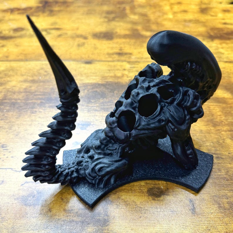 Puede incluir: Una figura de criatura alien&iacute;gena negra impresa en 3D con una cola larga y segmentada. La criatura tiene una superficie detallada y texturizada y una boca grande y abierta.