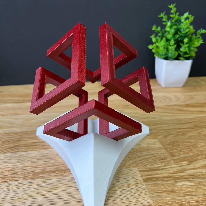 以下が含まれることがあります： 白い台座の上に置かれた赤い3Dプリントの幾何学的な彫刻。彫刻は、4つの側面が開いて星形になっている立方体です。