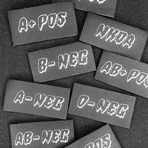 May include: Ten black rectangular labels with white text indicating different blood types and Rh factors. The labels read: O+ POS, A+ POS, B- NEG, AB+ POS, A- NEG, O- NEG, AB- NEG, B+ POS, and NKOA.