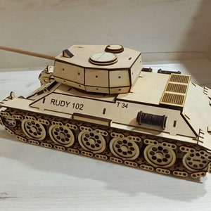 Puede incluir: Un kit de modelo de madera de un tanque T-34, un tanque medio sovi&eacute;tico utilizado durante la Segunda Guerra Mundial. El modelo no est&aacute; pintado y presenta piezas detalladas, incluida la torreta, las orugas y el ca&ntilde;&oacute;n. El modelo est&aacute; etiquetado como "RUDY 102" y "T 34".