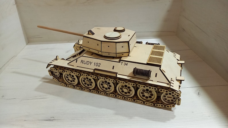 Puede incluir: Un kit de modelo de madera de un tanque T-34, un tanque medio sovi&eacute;tico utilizado durante la Segunda Guerra Mundial. El modelo no est&aacute; pintado y presenta piezas detalladas, incluida la torreta, las orugas y el ca&ntilde;&oacute;n. El modelo est&aacute; etiquetado como "RUDY 102" y "T 34".