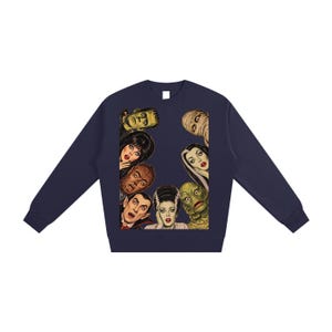 Puede incluir: Una sudadera azul marino de manga larga con un estampado gráfico rectangular de personajes clásicos de películas de terror, incluyendo el monstruo de Frankenstein, una momia, un vampiro y un hombre lobo dispuestos en un borde central.