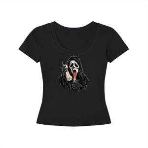 Puede incluir: Una camiseta negra de manga corta con un estampado gráfico de una figura encapuchada con máscara blanca, boca abierta con una lengua larga, sosteniendo un auricular de teléfono beige vintage en una mano y un encendedor encendido en la otra.