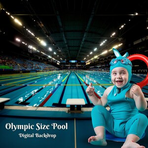 May include: A baby wearing a blue swimsuit and a bunny ear hat sits in front of an Olympic-sized swimming pool. The pool is empty and has lane markers. The baby is holding a red inflatable ring.