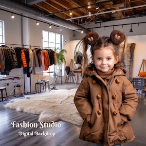 Może przedstawiać: Mała dziewczynka w brązowym zimowym płaszczu z dużymi guzikami i brązowymi futrzanymi nausznikami stoi w studiu fotograficznym z białym dywanem i stojakiem na ubrania w tle. Tekst "Fashion Studio - Digital Backdrop" jest widoczny na dole obrazu.