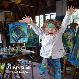 May include: A child covered in paint jumps in the air with arms raised in an art studio. The studio is filled with colorful paintings on easels and art supplies on a table.
