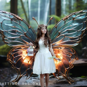 May include: A woman in a white dress stands in front of a large, illuminated, blue and gold butterfly sculpture. The sculpture has a delicate, intricate design and is lit from within, creating a warm glow.