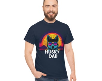 May include: Navy blue t-shirt featuring a graphic of a husky dog wearing sunglasses, set against a sunset backdrop. The text "HUSKY DAD" is printed below the dog. The shirt is made of a soft material.