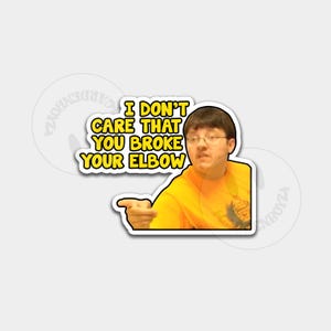 Puede incluir: Una pegatina con un hombre con una camisa amarilla y gafas señalando hacia la izquierda. La pegatina tiene el texto "I DON'T CARE THAT YOU BROKE YOUR ELBOW" en amarillo y negro.
