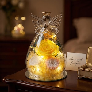 Könnte beinhalten: Eine Glasengel-Figur mit einer gelben Rose und anderen Blumen im Inneren. Der Engel hat klare Flügel und einen Heiligenschein. Die Basis ist ein Spiegelkreis, und die Karte lautet: "An angel for you..."