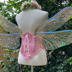 K&ouml;nnte beinhalten: Ein Paar regenbogenfarbene Feenfl&uuml;gel mit einem rosa Satin-Korsett. Die Fl&uuml;gel sind aus klarem Kunststoff mit einem zarten Muster und haben eine schimmernde Oberfl&auml;che.