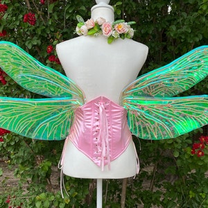 K&ouml;nnte beinhalten: Ein Paar regenbogenfarbene gr&uuml;ne Libellenfl&uuml;gel mit einem rosa Satin-Korsett. Die Fl&uuml;gel sind aus einem durchscheinenden Material mit einem zarten Adernmuster gefertigt.