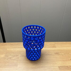 Puede incluir: Un portavasos azul vibrante con un dise&ntilde;o &uacute;nico de panal. El soporte est&aacute; hecho de un material duradero y presenta una serie de aberturas circulares espaciadas uniformemente. Est&aacute; dise&ntilde;ado para sostener una taza o vaso de tama&ntilde;o est&aacute;ndar. El soporte est&aacute; sobre una superficie de madera.