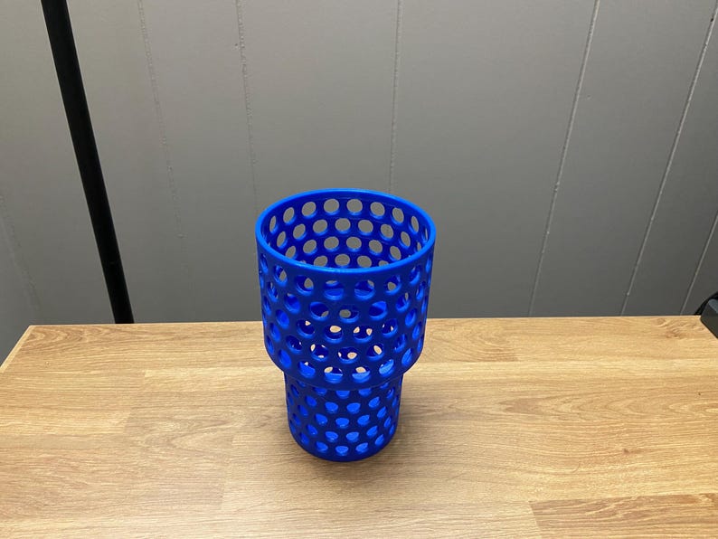 Puede incluir: Un portavasos azul vibrante con un dise&ntilde;o &uacute;nico de panal. El soporte est&aacute; hecho de un material duradero y presenta una serie de aberturas circulares espaciadas uniformemente. Est&aacute; dise&ntilde;ado para sostener una taza o vaso de tama&ntilde;o est&aacute;ndar. El soporte est&aacute; sobre una superficie de madera.