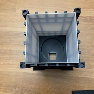 May include: A black and white 3D-printed lantern with a square shape. The lantern has a white interior with a grid pattern and a circular base with a square opening. The corners of the lantern have decorative elements.