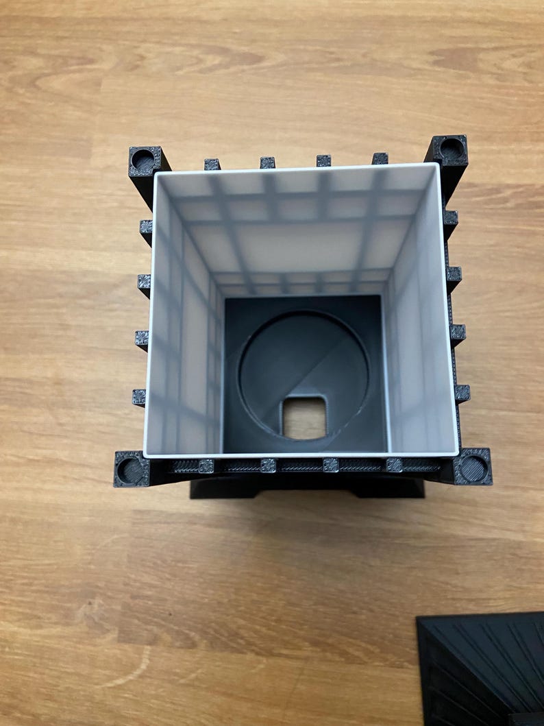 May include: A black and white 3D-printed lantern with a square shape. The lantern has a white interior with a grid pattern and a circular base with a square opening. The corners of the lantern have decorative elements.