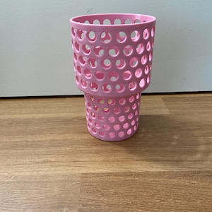 Puede incluir: Un portavasos rosa perforado con forma cil&iacute;ndrica. El portavasos tiene una serie de agujeros circulares espaciados uniformemente por todo su cuerpo. La base es ligeramente m&aacute;s peque&ntilde;a que la parte superior, creando un efecto escalonado. El art&iacute;culo es de pl&aacute;stico.