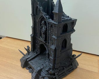 Puede incluir: Un modelo negro impreso en 3D de una catedral gótica en ruinas. El modelo presenta detalles intrincados, incluyendo ventanas arqueadas, una cruz en la cima de una torre y una apariencia desgastada. La estructura se asienta sobre una base con un puente y escombros.
