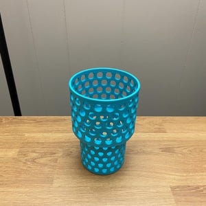 Puede incluir: Un portavasos turquesa con dise&ntilde;o de panal. El portavasos es de pl&aacute;stico y tiene forma cil&iacute;ndrica con una parte superior m&aacute;s ancha y una base m&aacute;s estrecha. Los agujeros est&aacute;n espaciados uniformemente.