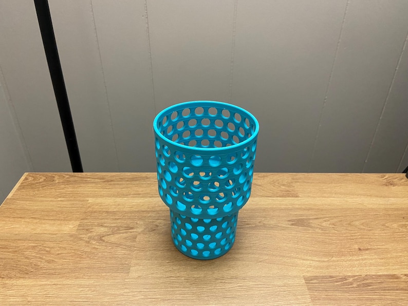 Puede incluir: Un portavasos turquesa con dise&ntilde;o de panal. El portavasos es de pl&aacute;stico y tiene forma cil&iacute;ndrica con una parte superior m&aacute;s ancha y una base m&aacute;s estrecha. Los agujeros est&aacute;n espaciados uniformemente.