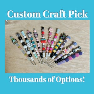 Puede incluir: Una variedad de pinchos artesanales personalizados coloridos con diferentes cuentas, dijes y diseños. Los pinchos están hechos con clavijas de madera y presentan una variedad de temas, que incluyen comida, animales y diseños abstractos. El texto "Custom Craft Pick" y "Thousands of Options!" está escrito en la imagen.