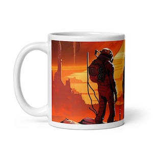 May include: White ceramic mug with a colorful illustration of two astronauts standing on a red planet with a large, orange sun in the background. The astronauts are wearing white spacesuits with red accents. The planet has a rocky surface and a city in the distance.