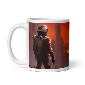 May include: White ceramic mug with a colorful image of an astronaut in a red and white spacesuit standing in front of a futuristic city. The astronaut is looking out at a red sky.