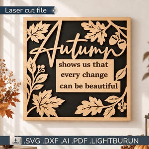 Puede incluir: Un letrero cuadrado de madera cortado con láser con fondo negro y marco de madera clara. El diseño incluye recortes intrincados de hojas de roble y bellotas. El texto dice: Autumn shows us that every change can be beautiful.