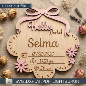Op de afbeelding: Houten lasergesneden bord met de tekst "Hello World" en de naam "Selma". Het bord bevat de datum 18/05/2026, gewicht 3450 gram en lengte 54 cm. Het heeft een roze strik en bloemaccenten.