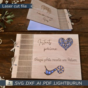 Peut inclure: Un album photo en bois avec des motifs découpés au laser. La couverture porte les inscriptions « Instants précieux » et « Chaque photo raconte une histoire ». Un cœur bleu et une bobine de film sont également visibles. L'album est relié par une ficelle.