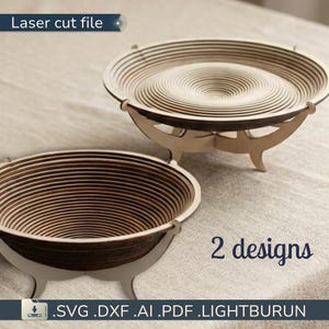 Peut inclure: Deux bols en bois découpés au laser avec un design en couches. Un bol est à l'endroit et l'autre est inversé. Les bols sont de couleur marron clair avec des bords marron foncé. Le texte "Laser cut file" et "2 designs" sont visibles.