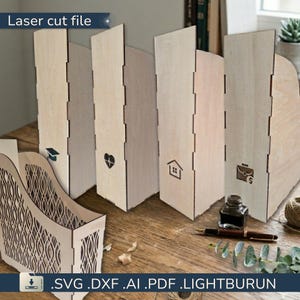 May include: Laser cut wooden file organisers with decorative cutouts and icons. The organisers are made of light-coloured wood and feature icons such as a graduation cap, heart, house, and briefcase. The text "Laser cut file" is visible.