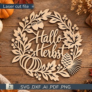 Può includere: Un cartello circolare in legno tagliato al laser con il testo Hallo Herbst al centro. Il design è circondato da una ghirlanda di foglie intagliate, ghiande, una zucca e una pigna. Il legno marrone chiaro ha una finitura liscia e intagli.