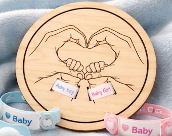 May include: A wooden laser-cut design featuring hands forming a heart shape, with the text "Baby boy" and "Baby Girl" on small tags. Includes blue and pink baby bracelets with the word "Baby". The text "Laser cut file" is visible.