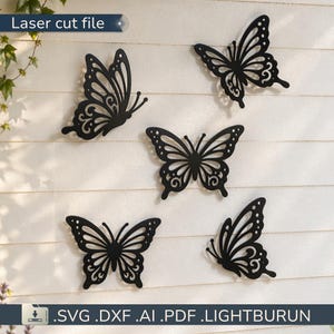 May include: Five black butterfly cutouts with detailed wing patterns are displayed against a white slatted backdrop. The text "Laser cut file" is at the top left. The bottom of the image shows file type options: .SVG .DXF .AI .PDF .LIGHTBURUN.
