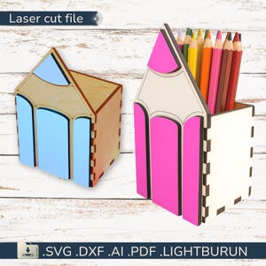 Puede incluir: Dos organizadores de escritorio de madera con forma de lápiz. Uno es de madera natural con detalles azules, el otro es blanco con detalles rosas y contiene lápices de colores. El texto "Laser cut file" y las extensiones de tipo de archivo son visibles.