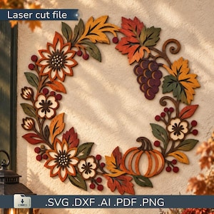 Può includere: Un file di taglio laser raffigurante una ghirlanda circolare composta da elementi autunnali in legno, tra cui girasoli, fiori, grappoli d'uva, una zucca e varie foglie nei toni dell'arancione, rosso, giallo e verde con il testo Laser cut file.