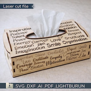 Puede incluir: Caja de pañuelos de madera con diseño cortado con láser. La caja rectangular tiene una abertura ovalada para los pañuelos. Los lados están decorados con palabras como "Inspiración", "Coraje" y "Sonrisa".