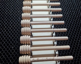 Puede incluir: Una colección de cucharas para miel de madera, cada una con una cabeza ranurada y un mango largo. Las cucharas están dispuestas verticalmente, descansando sobre una base de madera clara. El texto "Laser cut file" es visible en la parte superior.