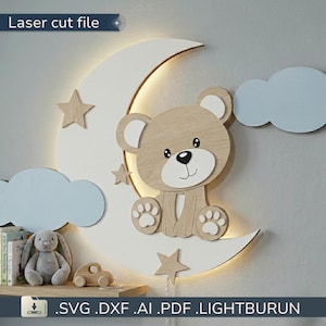 Pode incluir: Uma luminária de parede com uma lua crescente branca, um urso de madeira castanho claro, três estrelas de madeira e duas nuvens azul claro. O texto Laser cut file e SVG.DXF.AI.PDF.LIGHTBURUN é visível na imagem.