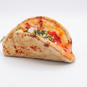 Op de afbeelding: Een taco-vormig etui met ritssluiting. De etui is ontworpen om op een volledig gevulde taco te lijken, met een getextureerde, bruine tortilla en kleurrijke vullingen van rood, wit en groen. De rits is goudkleurig.