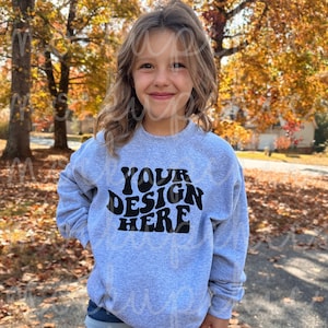 May include: A gray sweatshirt with the text "YOUR DESIGN HERE" in black, retro-style lettering. The sweatshirt is being worn by a child standing outdoors.
