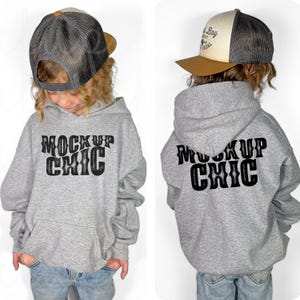 Puede incluir: Una sudadera gris con capucha con un gráfico negro "Mock Up Chic" en la parte delantera y trasera. La sudadera tiene capucha y bolsillo canguro. El modelo lleva una gorra de béisbol gris y marrón.