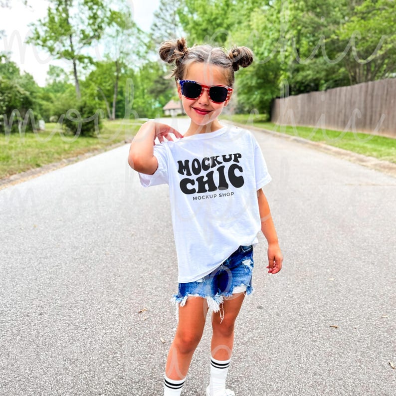May include: A young person wearing a white t-shirt with the text "MOCKUP CHIC" and the words "MOCKUP SHOP" underneath. The person is wearing denim shorts and sunglasses.