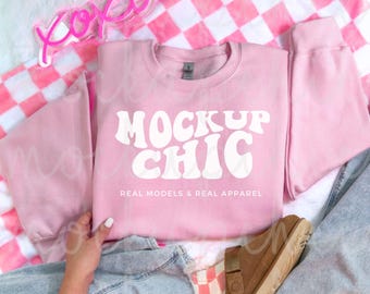 May include: Pink sweatshirt with the text "Mock Up Chic" in white, with the words "Real Models & Real Apparel" below. The sweatshirt is laid out on a checkered pink and white blanket.