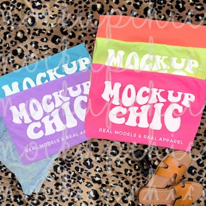 May include: A collection of colorful t-shirts with the text "MOCKUP CHIC" in white. The shirts are in shades of blue, purple, pink, green, and orange. The phrase "REAL MODELS & REAL APPAREL" is also visible.