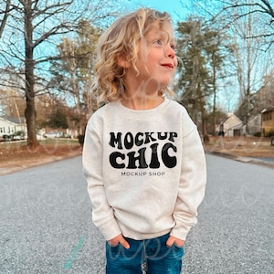 Może przedstawiać: Dziecko w jasnobeżowej bluzie z czarnym napisem "MOCKUP CHIC MOCKUP SHOP".