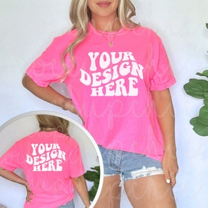 May include: A bright pink t-shirt with the text "YOUR DESIGN HERE" in a white retro font. The shirt is shown on a model wearing denim shorts.