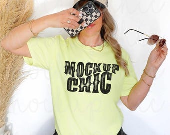 Op de afbeelding: Een vrouw draagt een neon geel t-shirt met de tekst "Mock Up Chic" in zwart. Ze draagt een zwarte bucket hat met de tekst "The Mock Club Collective" en een zonnebril.